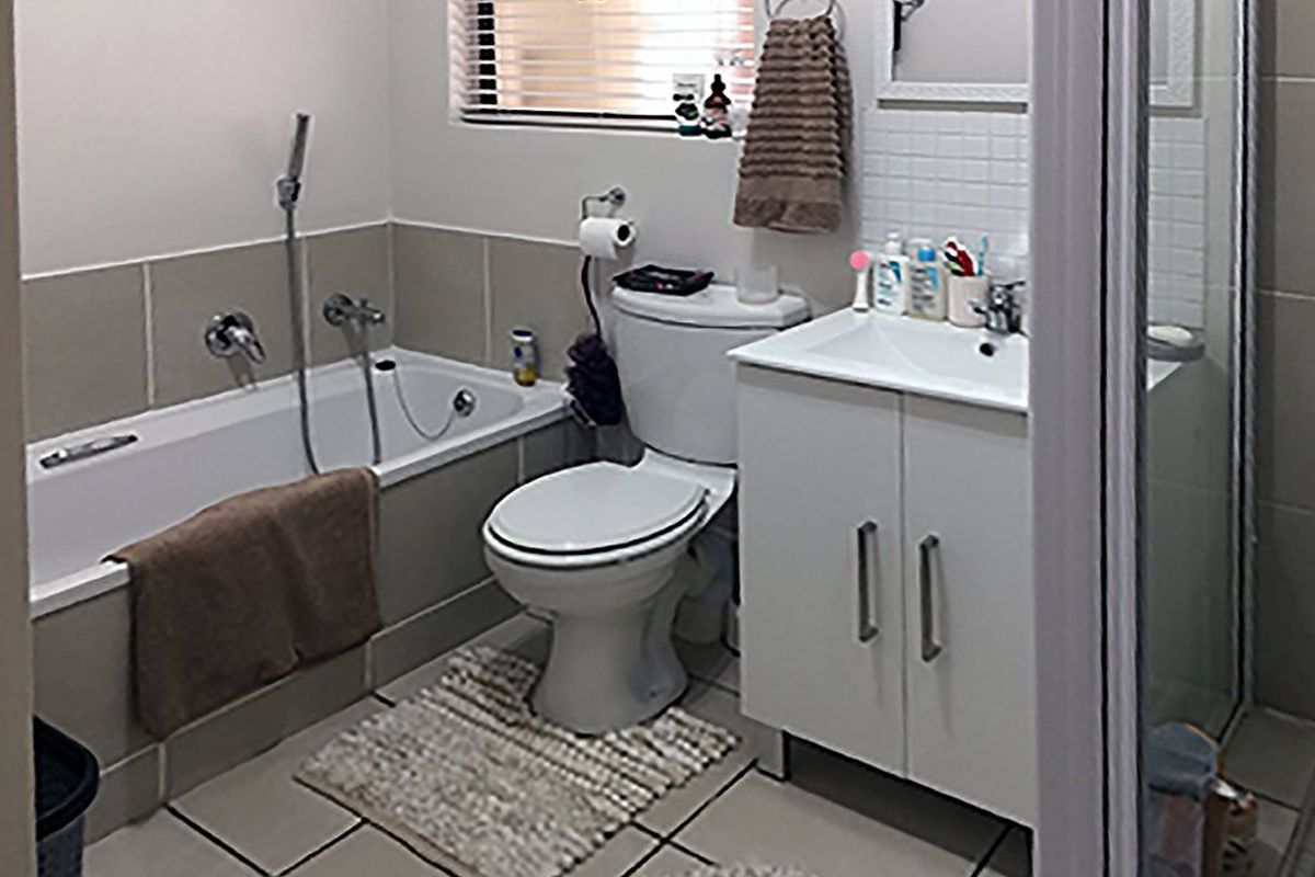 A functional bathroom featuring a built-in bathtub, separate shower enclosure, vanity cabinet with basin, and neutral wall and floor tiling.