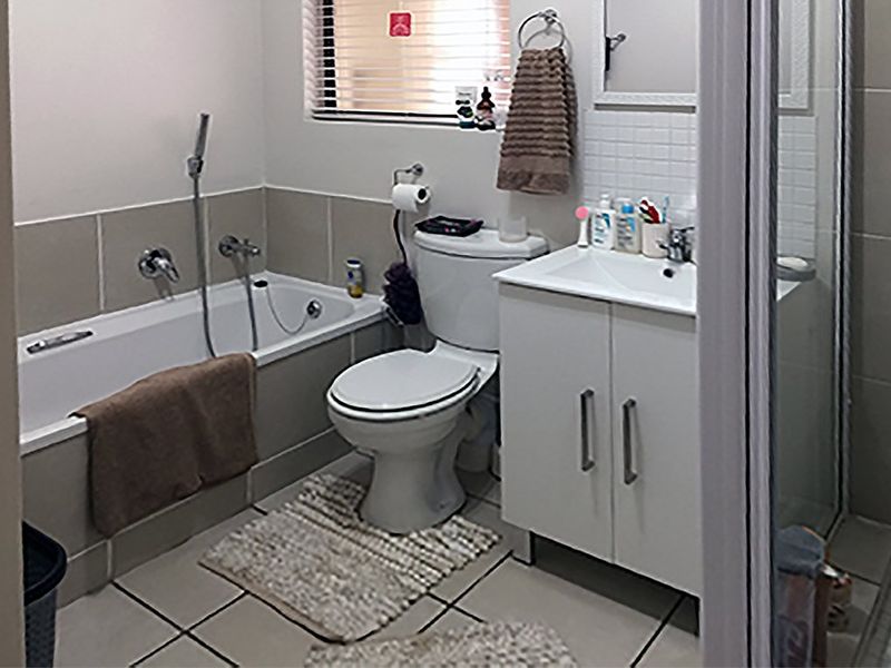 A functional bathroom featuring a built-in bathtub, separate shower enclosure, vanity cabinet with basin, and neutral wall and floor tiling.