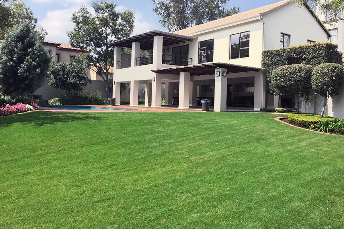 Rear view of the property featuring a spacious lawn, swimming pool, and a covered patio area with an upper-level balcony.