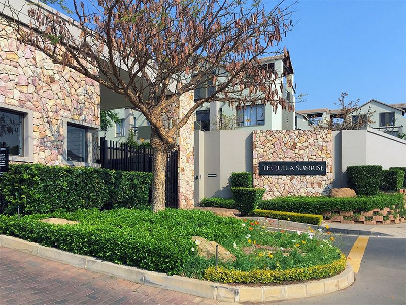 The entrance to Tequila Sunrise apartment complex featuring stone-clad boundary walls, secure gated access, and well-maintained landscaped gardens.