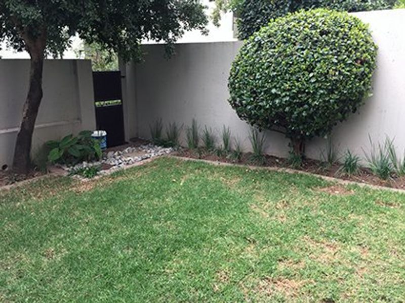 A private garden area featuring a well-maintained lawn, established shrubbery, and a secure boundary wall with a metal access gate.