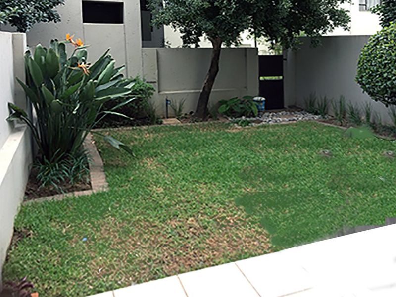A private enclosed garden area featuring a lawn, established trees, and a paved border, accessible via a rear pedestrian gate.