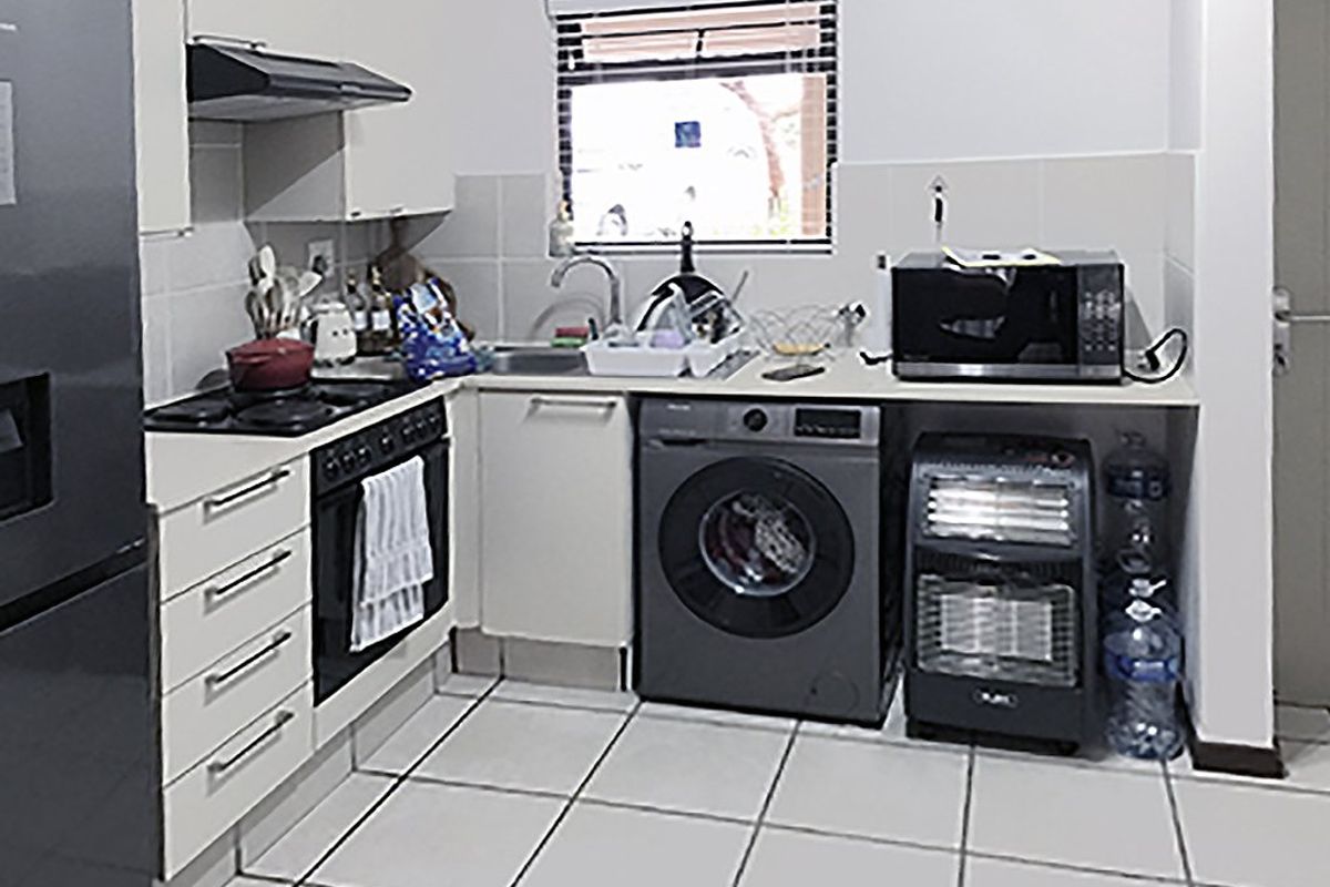 Compact kitchen featuring white cabinetry, tiled flooring, a built-in oven with hob, extractor fan, and integrated space for laundry appliances.