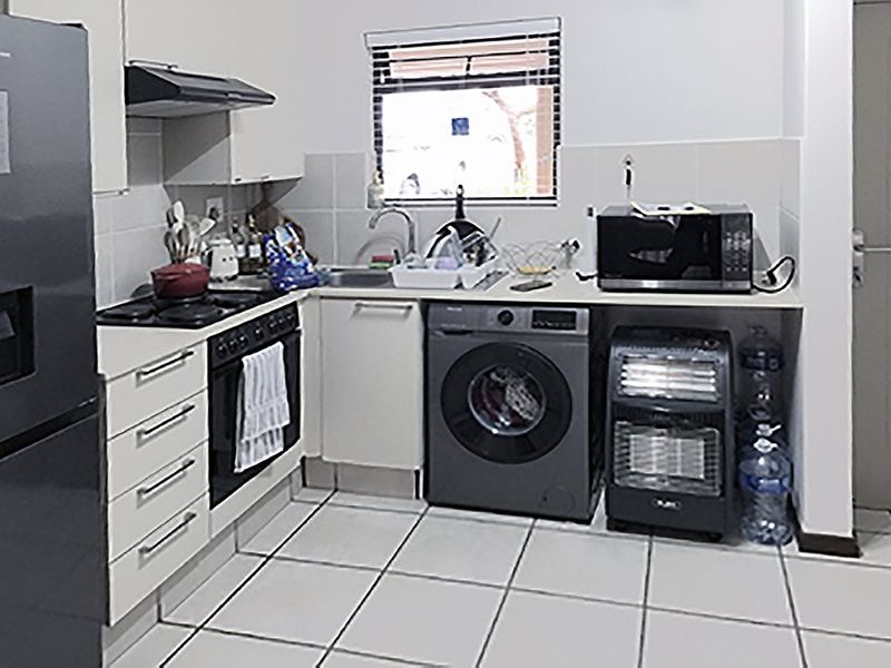Compact kitchen featuring white cabinetry, tiled flooring, a built-in oven with hob, extractor fan, and integrated space for laundry appliances.