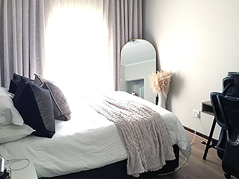 A well-lit bedroom featuring laminate flooring and neutral wall finishes, providing a comfortable and functional living space.