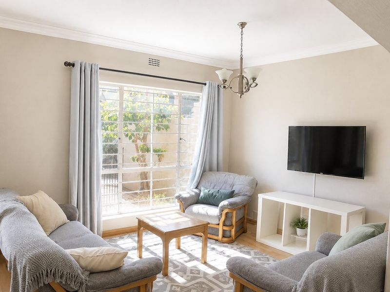 A bright and comfortable living room featuring laminate flooring, a large window with security bars, and a classic chandelier.