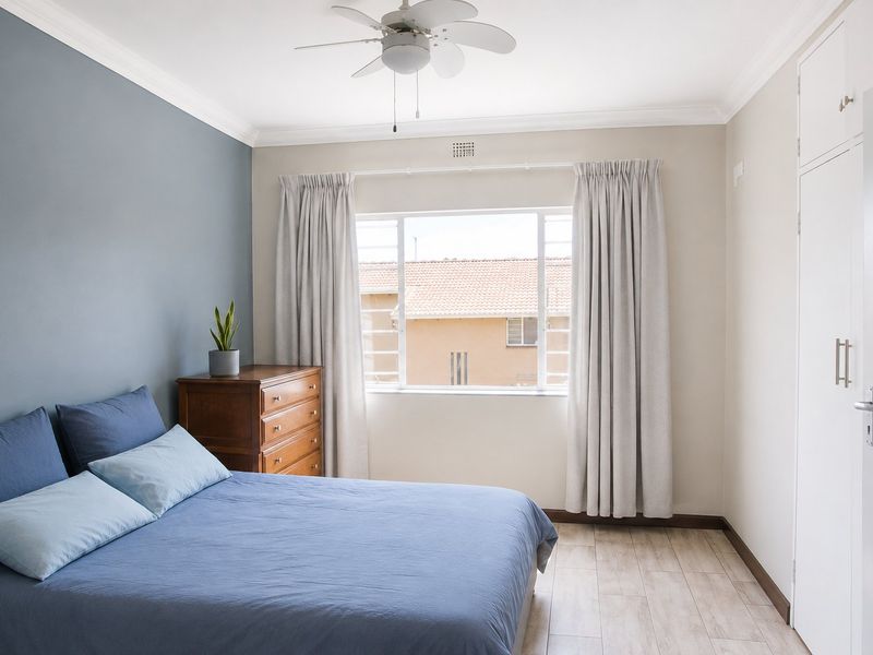 A well-maintained bedroom featuring tiled flooring, built-in cupboards, a ceiling fan, and a feature wall with neutral tones.