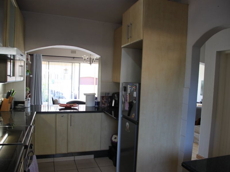 A functional kitchen featuring light wood cabinetry, dark granite countertops, and tiled flooring, with an open-plan layout leading to the living area.