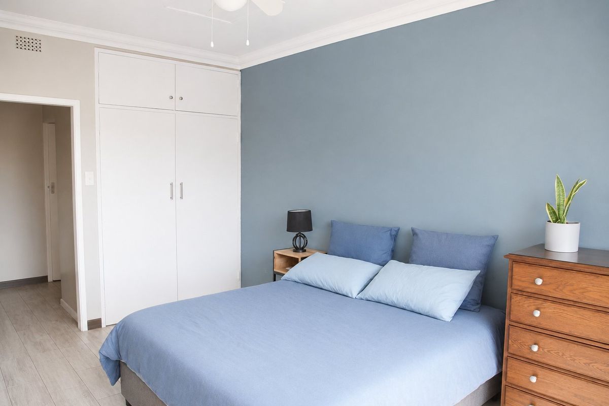 A well-maintained bedroom featuring a built-in wardrobe, ceiling fan, and neutral laminate flooring with a blue accent wall.