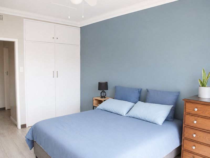 A well-maintained bedroom featuring a built-in wardrobe, ceiling fan, and neutral laminate flooring with a blue accent wall.