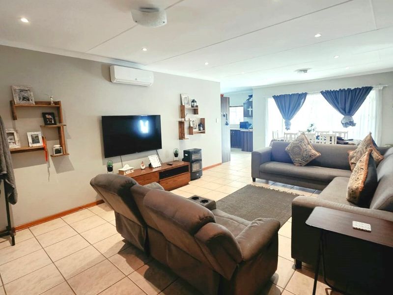 Spacious open-plan living area featuring tiled flooring, recessed lighting, and a wall-mounted air conditioning unit, flowing into the adjacent dining and kitchen space.