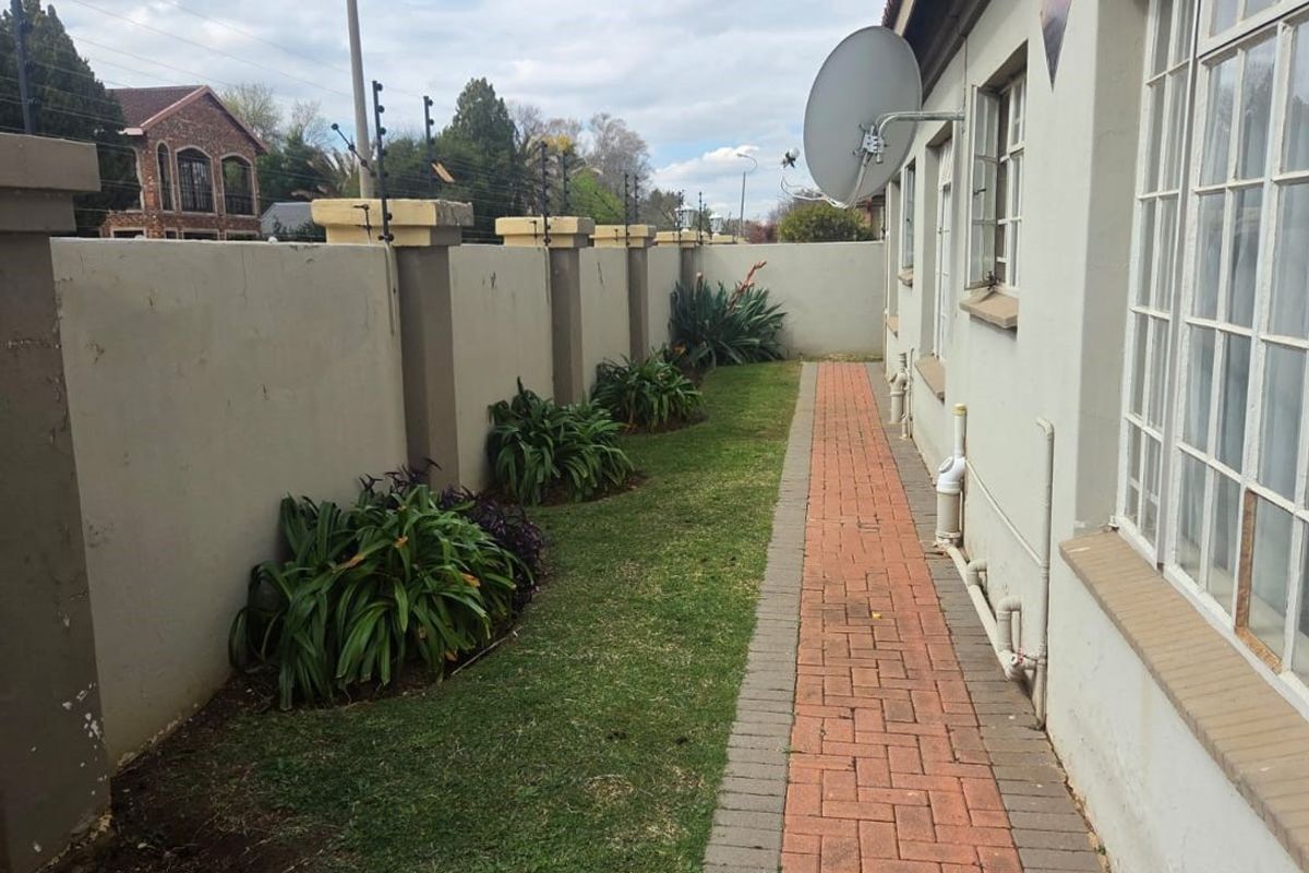 A side exterior view of the townhouse featuring a brick paved walkway, lawn, perimeter wall with electric fencing, and a satellite dish.
