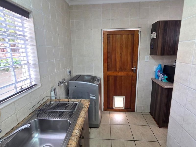 Functional laundry area featuring tiled walls and flooring, granite countertops, double stainless steel sink, and direct access to the exterior via a timber door.