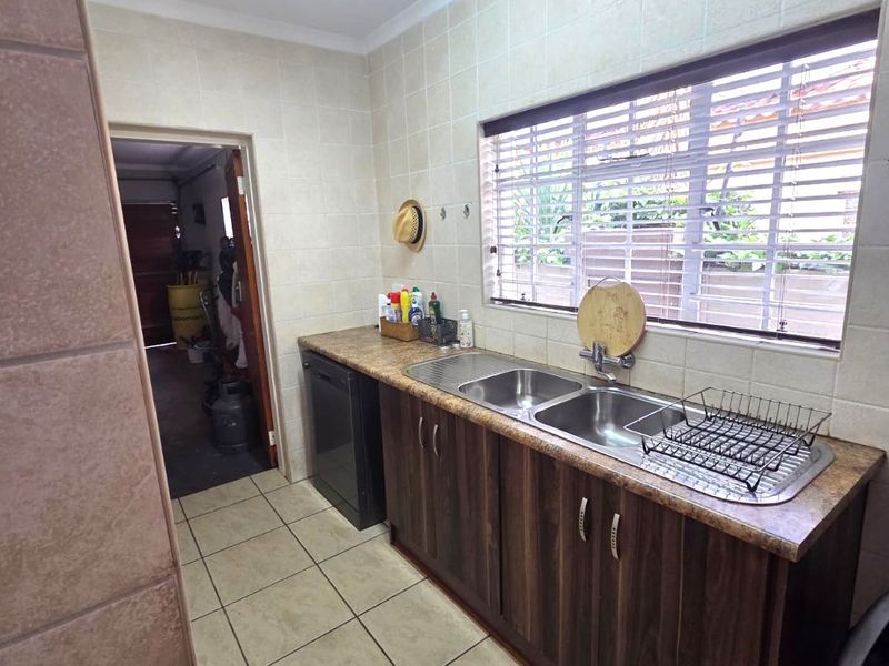 Functional scullery area featuring a double basin sink, laminate countertops, built-in cabinetry, and tiled finishes, providing practical utility space.