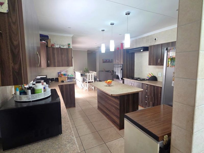 Spacious open-plan kitchen featuring dark wood cabinetry, stone countertops, a central island, and integrated appliances, flowing into the dining and living areas.