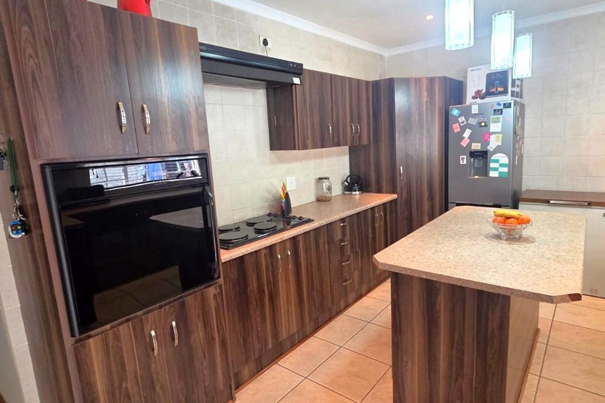 A functional kitchen featuring dark wood-look cabinetry, a central island, built-in oven, hob, and tiled finishes throughout.