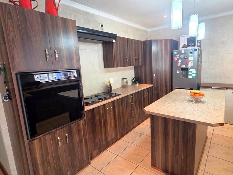 A functional kitchen featuring dark wood-look cabinetry, a central island, built-in oven, hob, and tiled finishes throughout.