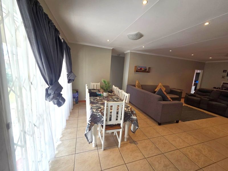 Spacious open-plan living and dining area featuring neutral tiled flooring, recessed downlighting, and large sliding glass doors with security gates.