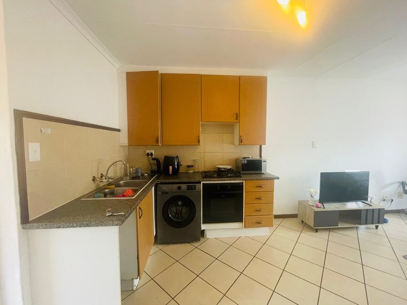 Open-plan kitchen area featuring built-in cabinetry, laminate countertops, integrated oven and hob, and tiled flooring, seamlessly connected to the living space.