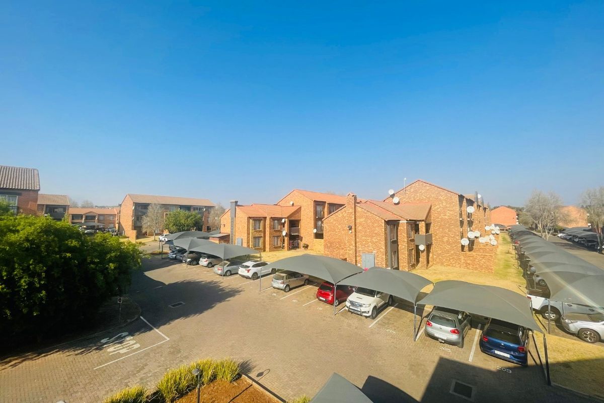 An elevated view of an apartment complex featuring brick buildings, paved parking areas, and covered shade cloth carports.