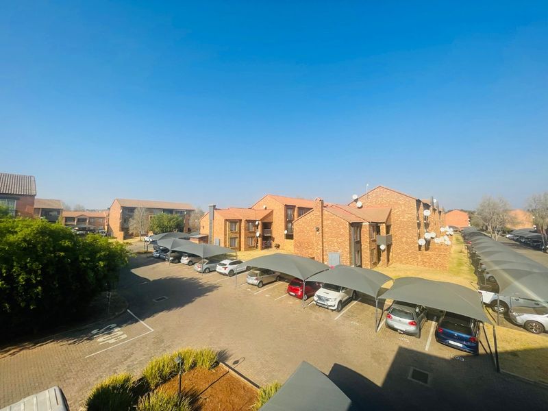 An elevated view of an apartment complex featuring brick buildings, paved parking areas, and covered shade cloth carports.