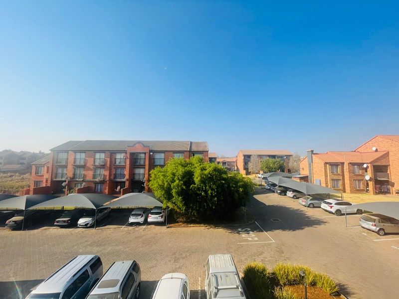 An elevated view of the apartment complex exterior, featuring paved parking areas with covered carports and multi-story brick residential buildings.