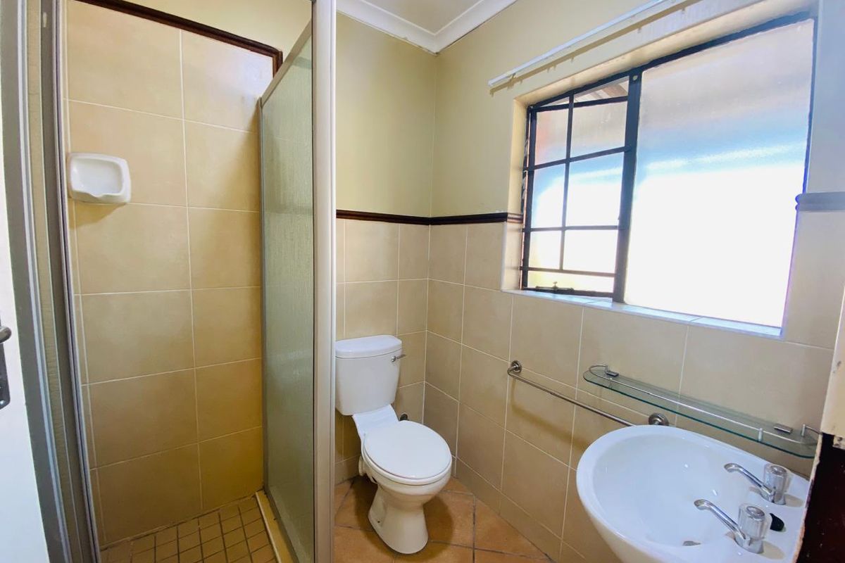 A functional bathroom featuring a shower enclosure, pedestal basin, and toilet with neutral wall tiling and natural light from a window.