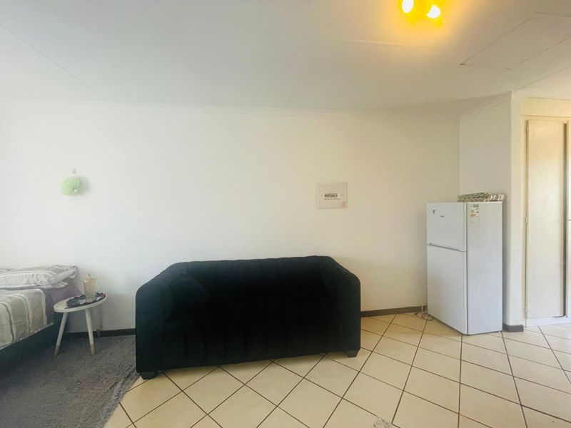 An open-plan living area featuring tiled flooring and a wall-mounted electrical distribution board, providing a functional and versatile space.