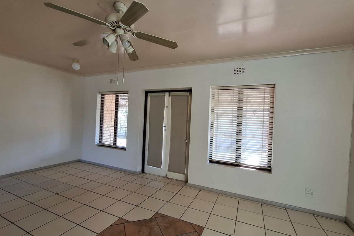 An empty living room featuring tiled flooring, a ceiling fan, and natural light through windows fitted with security bars and venetian blinds.