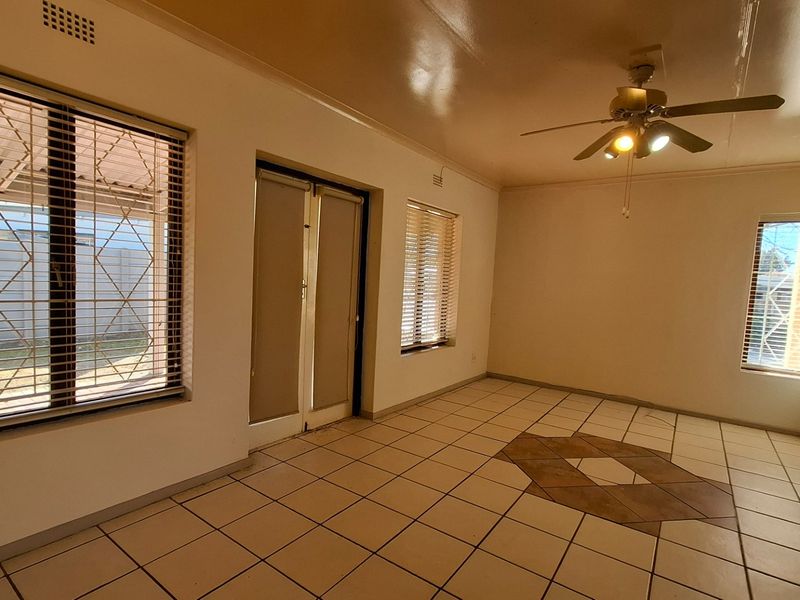 Spacious living area featuring tiled flooring, a ceiling fan, and large windows with security bars, offering a bright and open layout.