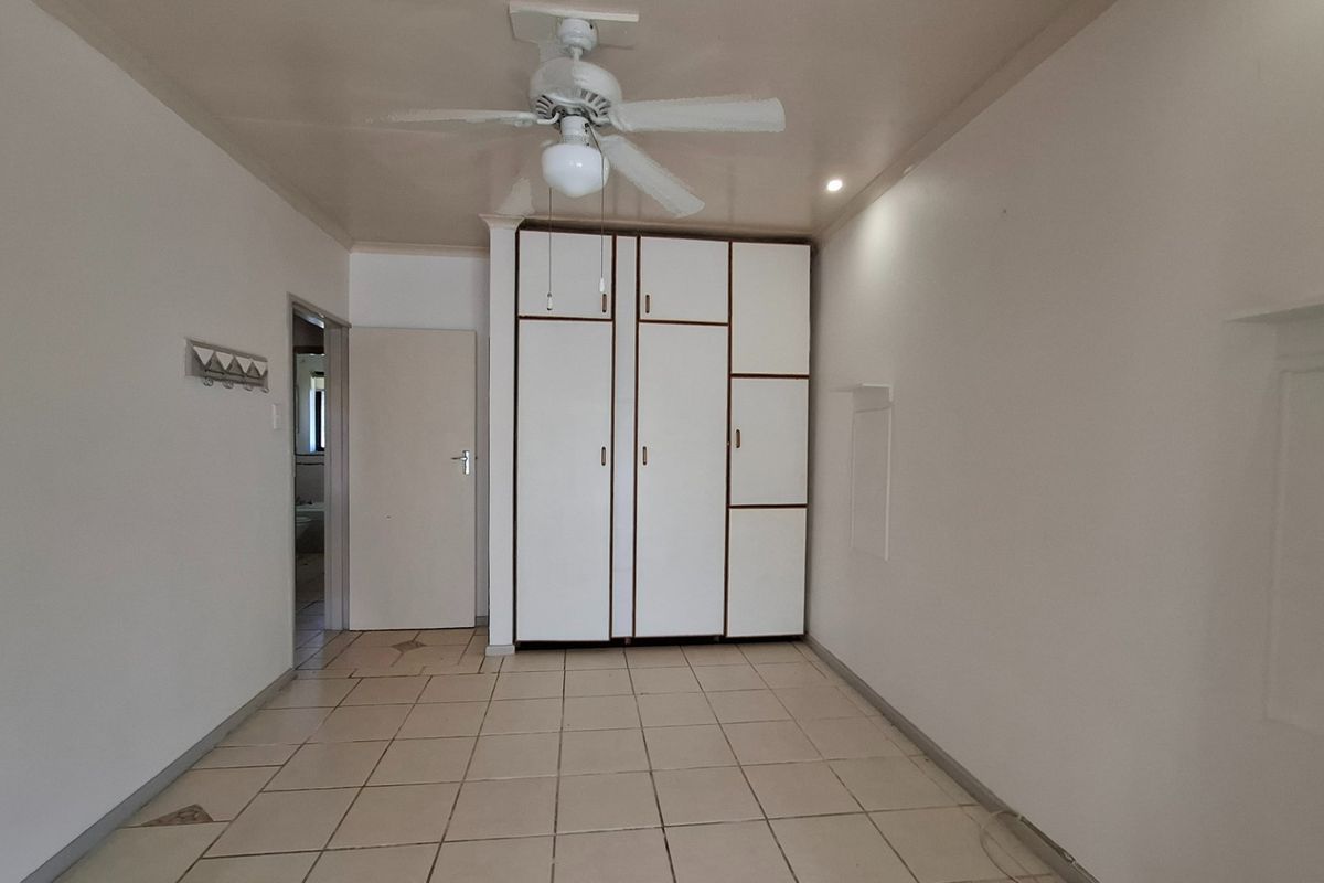 An empty bedroom featuring built-in cupboards, a ceiling fan, and tiled flooring, offering a neutral space ready for personalization.