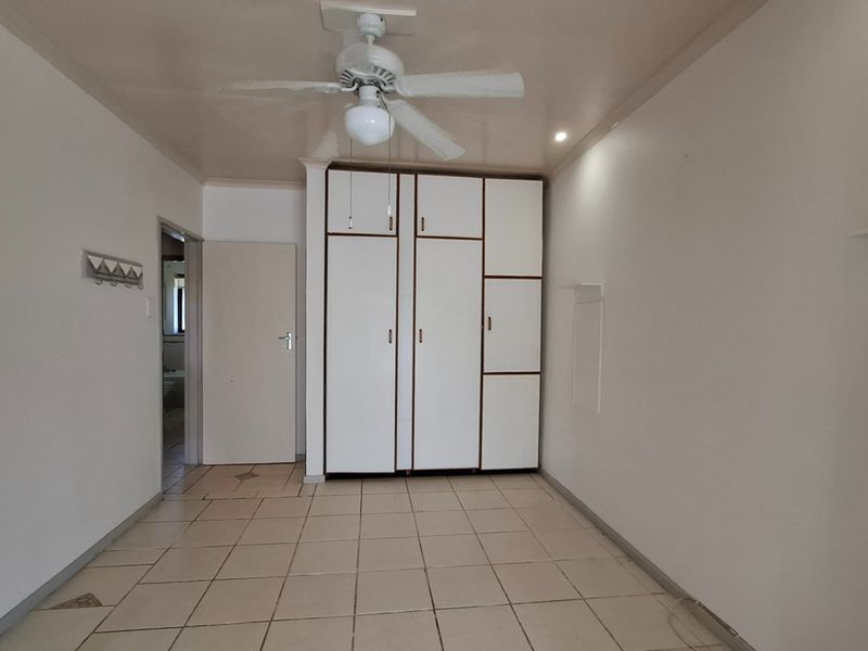 An empty bedroom featuring built-in cupboards, a ceiling fan, and tiled flooring, offering a neutral space ready for personalization.