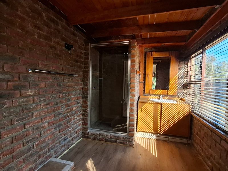 A rustic bathroom featuring exposed brick walls, timber ceiling beams, a shower enclosure, and a wooden vanity unit with an integrated basin.