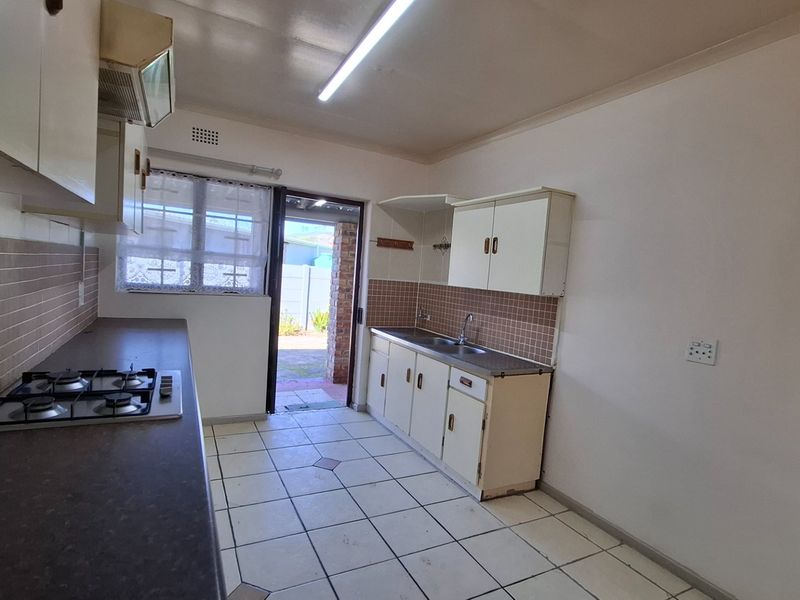 A functional, empty kitchen featuring built-in cabinetry, a gas hob, double sink, and tiled flooring with direct access to the rear exterior.