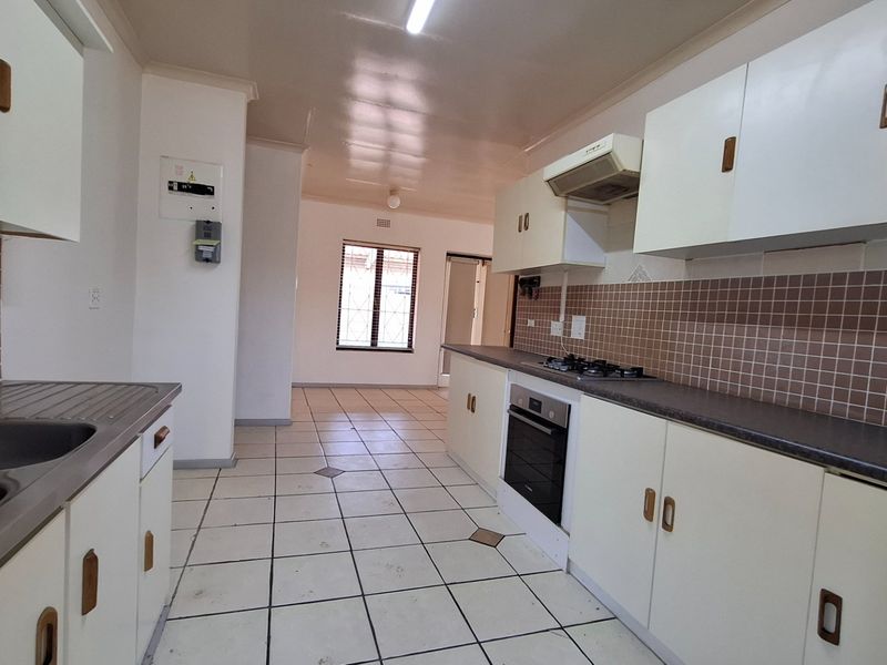 A functional kitchen featuring built-in cabinetry, a gas hob, oven, extractor fan, and tiled finishes, leading into an open-plan living area.
