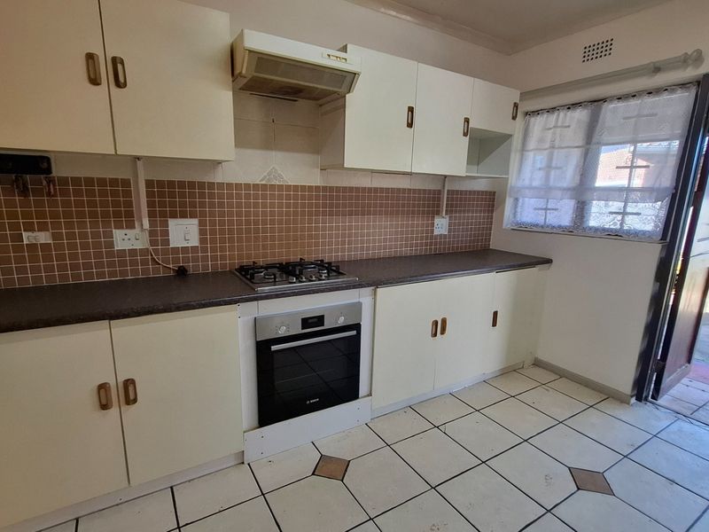 A functional kitchen featuring built-in cabinetry, a gas hob, an integrated oven, and a tiled backsplash with direct access to the exterior.