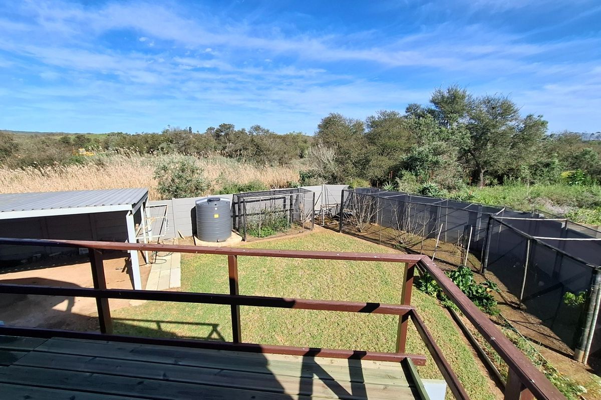 Elevated wooden deck overlooking a rear garden featuring a water tank, covered patio area, and fenced garden enclosures with natural landscape views.