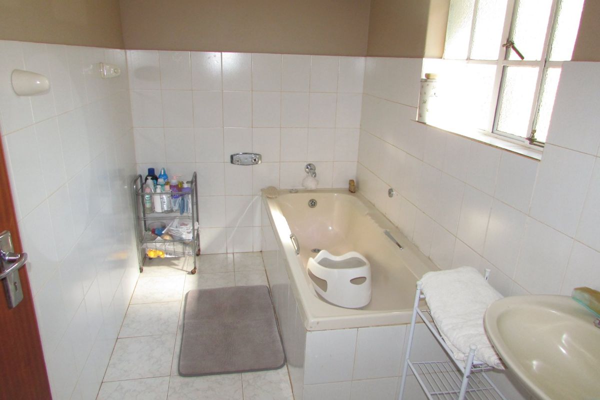 A functional bathroom featuring a built-in bathtub, wall-mounted basin, and tiled finishes. The space would benefit from modern updates to fixtures and finishes.