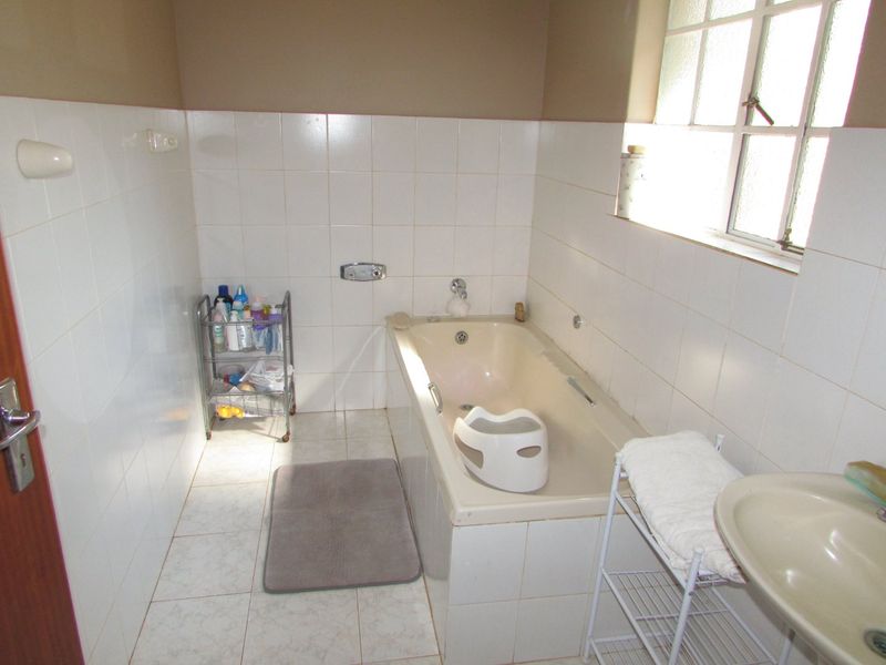 A functional bathroom featuring a built-in bathtub, wall-mounted basin, and tiled finishes. The space would benefit from modern updates to fixtures and finishes.