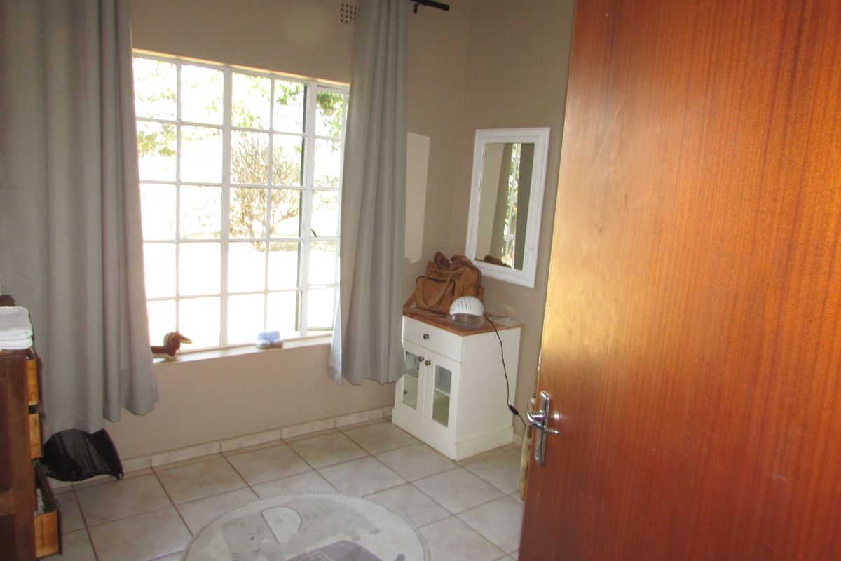 A bedroom featuring tiled flooring, a grid-pattern window, and a wooden door, providing a functional space with neutral wall tones.