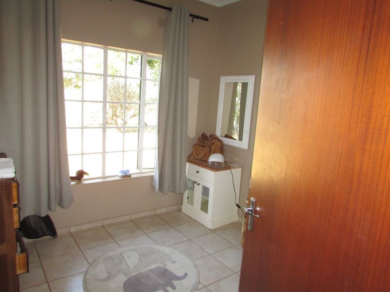 A bedroom featuring tiled flooring, a grid-pattern window, and a wooden door, providing a functional space with neutral wall tones.