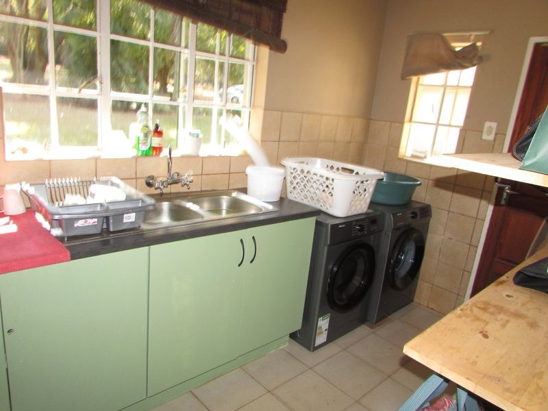 A functional laundry room featuring a double basin sink, tiled splashback, built-in cabinetry, and dedicated space for laundry appliances.