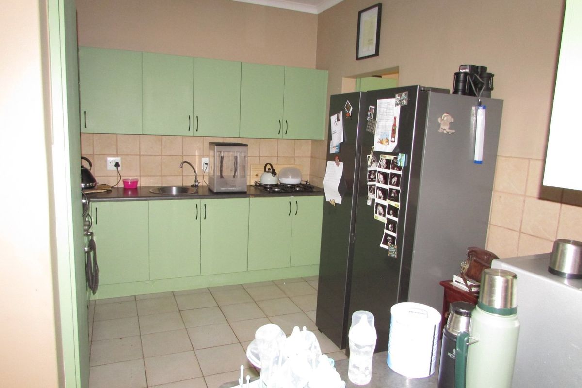 A functional kitchen featuring light green cabinetry, laminate countertops, a tiled backsplash, and ceramic floor tiles.