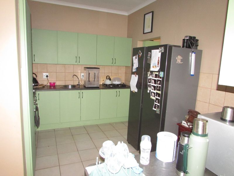 A functional kitchen featuring light green cabinetry, laminate countertops, a tiled backsplash, and ceramic floor tiles.