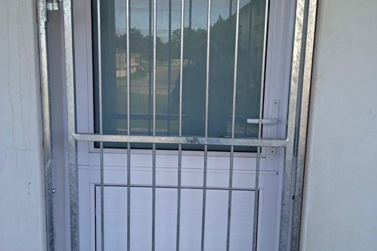 A secure exterior entrance featuring a white uPVC door with a frosted glass panel and a galvanized steel security gate.