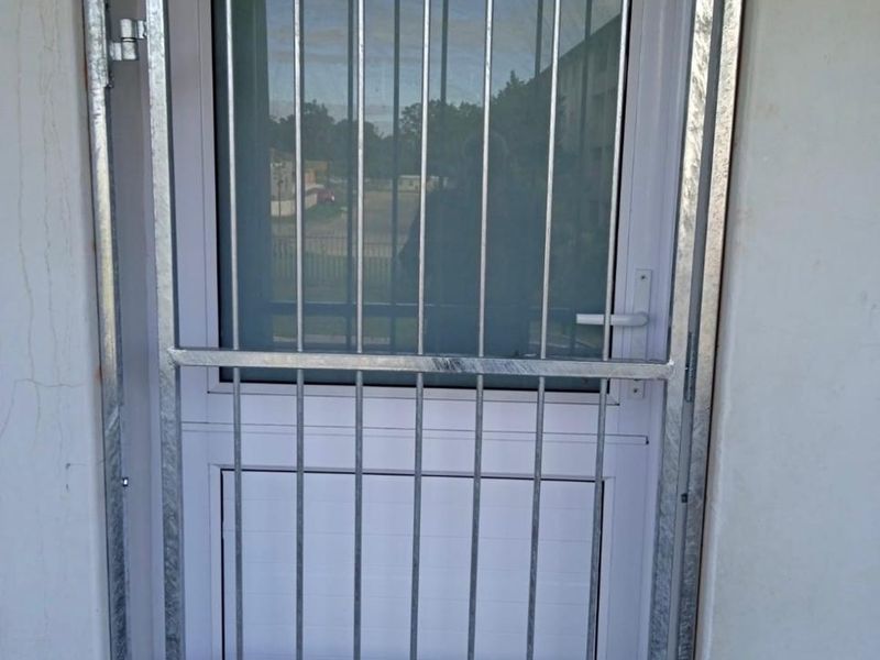 A secure exterior entrance featuring a white uPVC door with a frosted glass panel and a galvanized steel security gate.