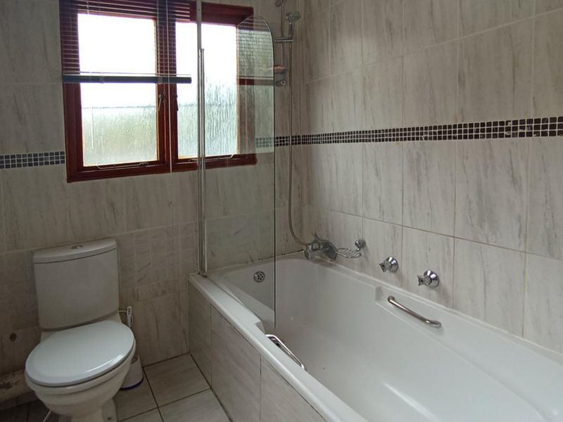 A functional bathroom featuring a bathtub with a glass shower screen, tiled walls, and standard sanitary fixtures.