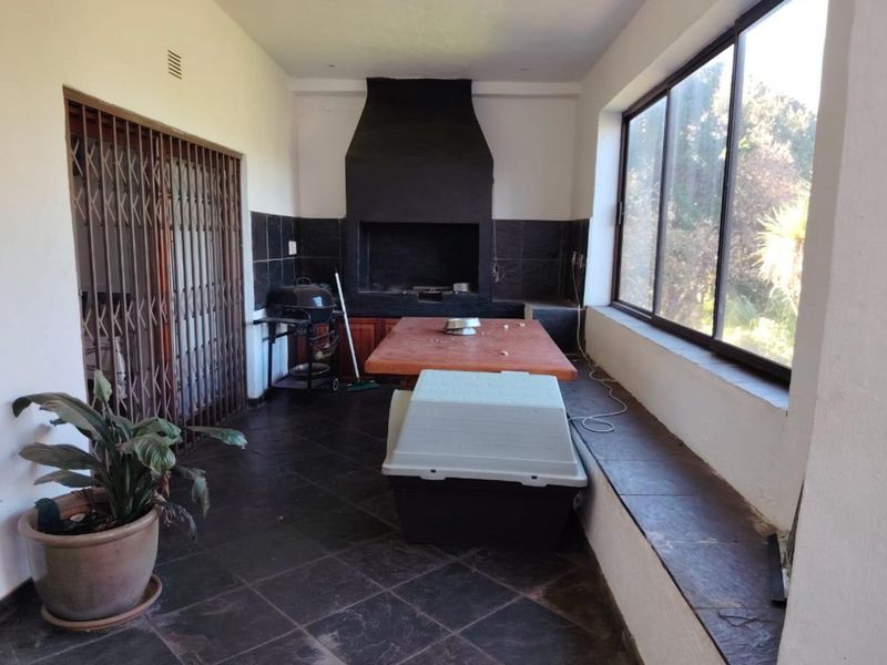 Covered patio area featuring a built-in braai, tiled flooring, and large windows overlooking the garden.