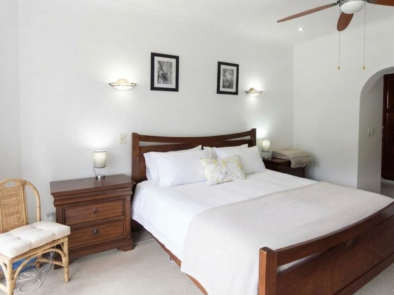 A well-maintained bedroom featuring neutral carpeting, a ceiling fan, recessed lighting, wall sconces, and an arched doorway leading to an adjoining space.