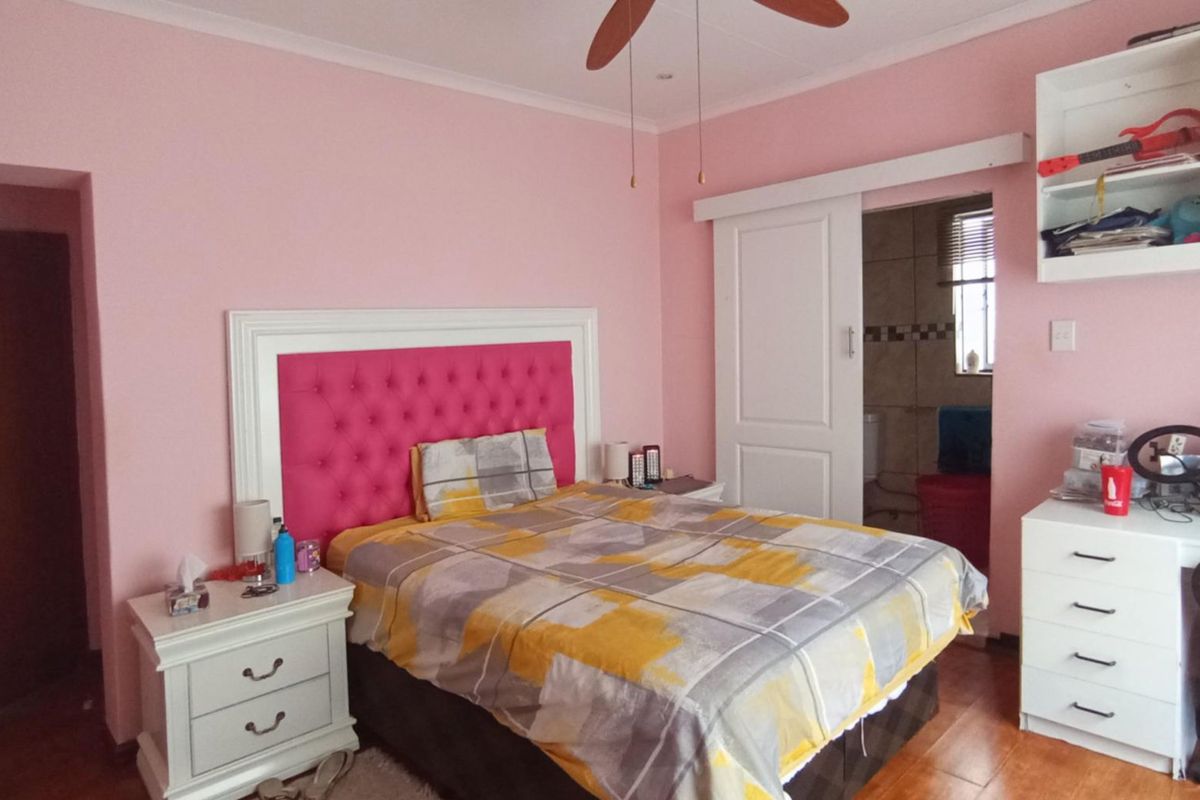 A bedroom featuring hardwood flooring, a ceiling fan, and a sliding door leading to an en-suite bathroom with built-in shelving.